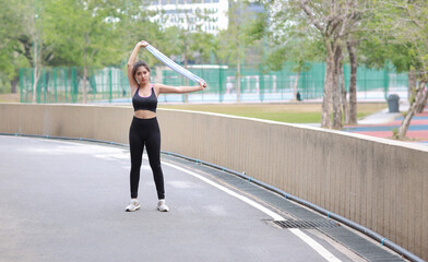 Portrait of sporty young asian woman in sportswear jogging outdoor for marathon training. Jogger girl stretching along concrete path outdoor with green tree background. Sport concept