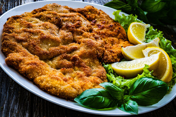 Breaded fried pork chop with lemon and fresh vegetables on wooden table
