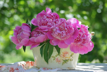 Bright bouquet of fresh pink peonies on the background of the blurred green of the sunny summer garden. Still life with flowers. Selective focus.