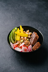 quinoa with juicy vegan cutlet, cucumber, radish, mini corn and chickpeas on a dark background