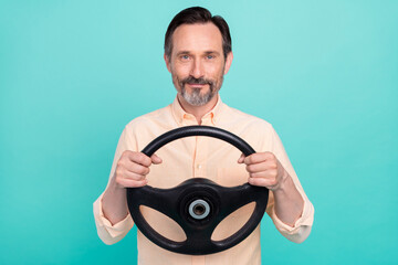 Portrait of mature good looking smiling taxi driver guy riding card hold steering wheel isolated on teal color background