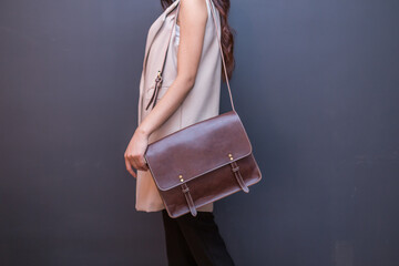 Woman carries brown leather messenger bag in the hand