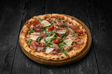 pizza with meat, parmesan and tomatoes on a wooden board on a dark table
