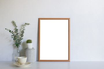 A blank picture frame with leaves on table.