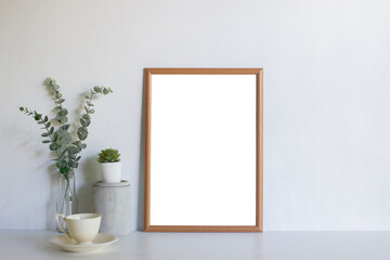 A blank picture frame with leaves on table.