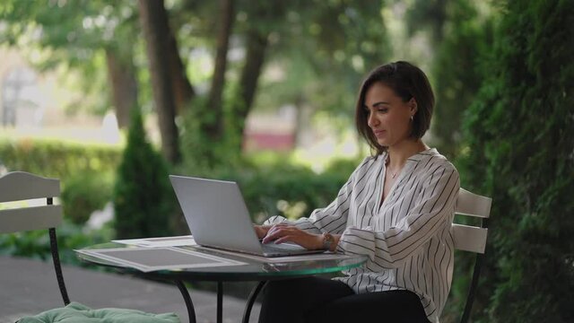 Business Woman Brunette arabic Hispanic ethnic group is typing on a laptop while sitting at a table in a summer cafe doing remote work. Freelancer woman. Small business