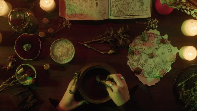 Witch cooking potion elixir top view. Table with spellbook for making rite. Herbs, burning candles, crystal magic ball for sacrifice. Halloween theme, full moon, witchcraft. 