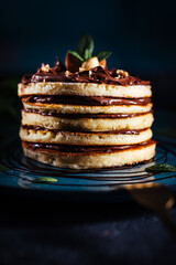 American pancakes with chocolate filling with mint and hazelnuts on a blue plate with dark background