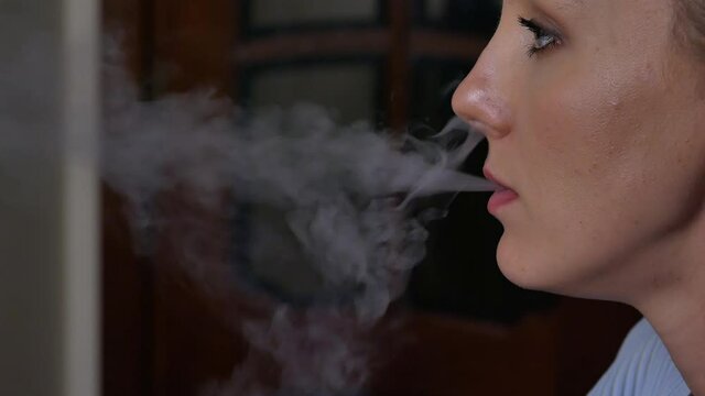 a girl smokes a hookah in the kitchen, exhales smoke