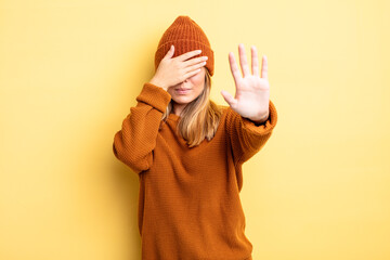 blonde pretty woman covering face with hand and putting other hand up front to stop camera,...