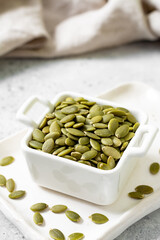 Pumpkin seeds in a white bowl on a light gray culinary background closeup	