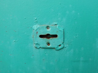 Vintage lock on green old  rusty door, construction and  security. A corroded metal blue keyhole. 