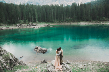 Wedding couple on the nature is hugging each other near a beautiful lake in the mountains.. Beautiful model girl in white dress. Man in suit