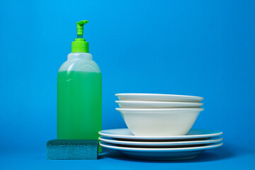 Detergent next to clean plates on a blue background. Ecological household chemicals