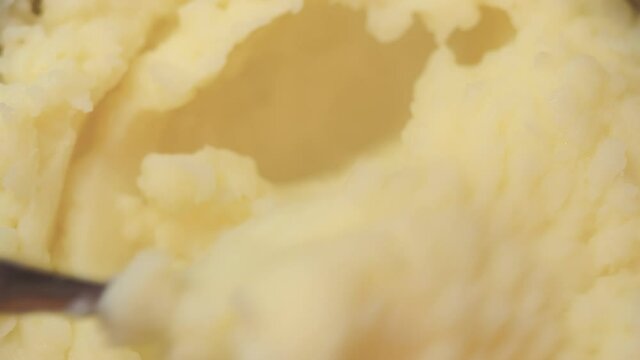 Hand using a fork to stir hot mashed boiled potatoes in a pan