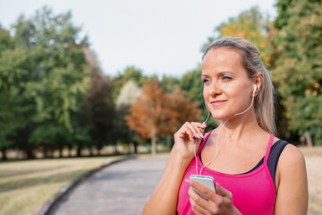 Beautiful mature blonde woman running at the park on a sunny day. Female runner listening to music while jogging.