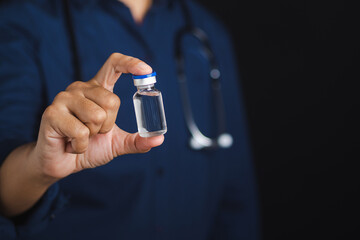 A doctor is holding a vaccine bottle while standing in the studio with a black background. Vaccine for prevention and treatment from virus infection. Concept of medical and the fight against the virus