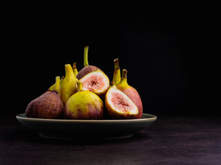A pile of ripe figs fruit on a plate with a black background. High Vitamins fruit. Close-up photo. Healthy fruits and healthcare concept