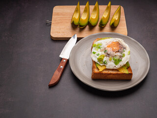 Toast with avocado and eggs served on a plate. Avocado sliced on a wooden cutting board with a knife. Top view. Space for text. High vitamin fruit. Healthy fruit concept