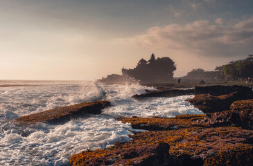 Pura Tanah Lot temple on clifftop and wave hitting on sunset beach in Bali