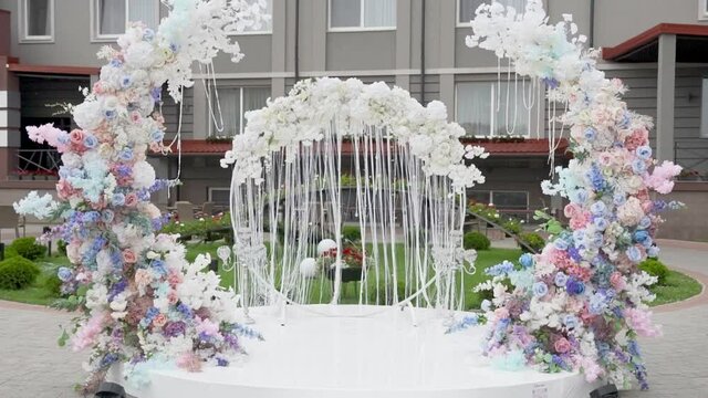 Beautiful exquisite round wedding arch made of fresh colorful flowers. Preparation for wedding ceremony. Organic flowers and shiny threads  sway in wind. Roses, peonies, hydrangeas and flowering stems