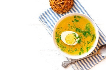 Homemade chicken broth with herbs and egg in a white bowl on a white background. Free space for text. Banner. Chicken soup.