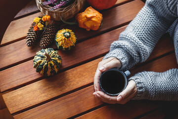 Enjoy strong black coffee. Woman holding mug of hot drink in cozy home interior with autumn decoration. Wooden table