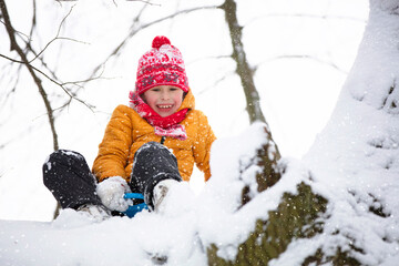 Funny little boy in colorful clothes playing outdoors during a snowfall. Active holidays with children in winter on cold snowy days. Happy child is having fun and playing in winter.