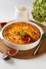 curd casserole with pumpkin in a round white shape on a wooden board to serve on a white table, vertical format