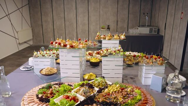 Exquisite expensive buffet with delicious snacks and cold cuts in stylish hall. Cossack table. Cossack buffet. Stacks and bottles of strong vodka on sides. Food on wooden boards and glass surfaces.