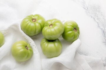 Green tomato for preservation on a white marble background. Unripe tomatoes for harvesting.