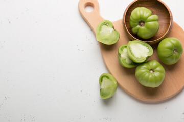 Green tomatoes for conservation on a wooden board on a gray background. Unripe tomatoes for harvesting. Cutaway tomato.