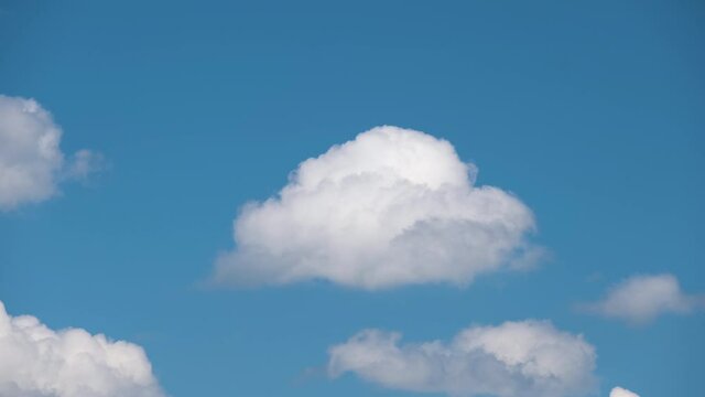 Time lapse footage of fast moving white puffy cumulus clouds on blue clear sky.