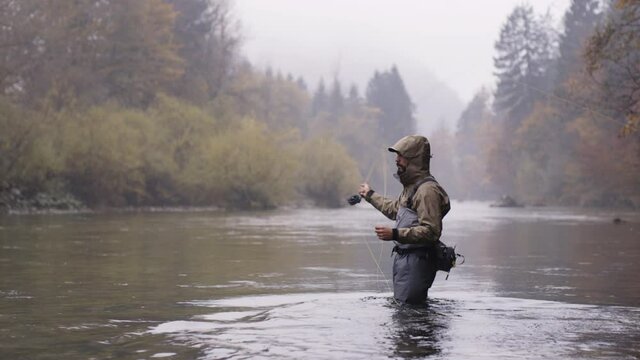 Man standing in the river with fishing rod, fly fishing on a autumn rainy day
