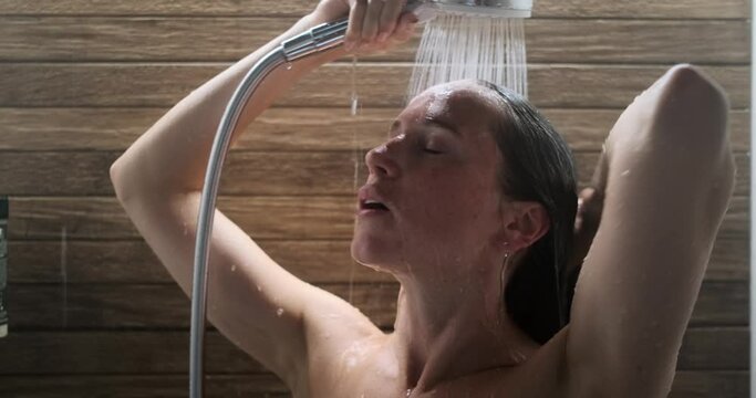Young woman bathing using hand shower in bathroom