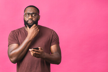 Fototapeta na wymiar Portrait of serious thinking african american guy wearing casual sending and getting messages to his lover isolated against pink background. Using phone.