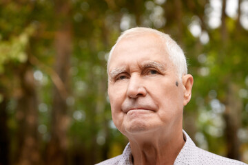 Porter of a gray-haired elderly man on a green background in the forest or in the park. Grandfather posing