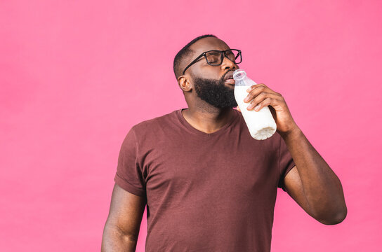 Portrait Of Young African American Black Man Holding Bottle Of Milk Isolated Over Pink Background. Healthy Food Concept.