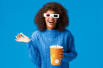 Happy amused good-looking african-american female laughing out loud, eating popcorn, watching comedy movie in 3d glasses, having fun, attend premiere in cinema, standing blue background