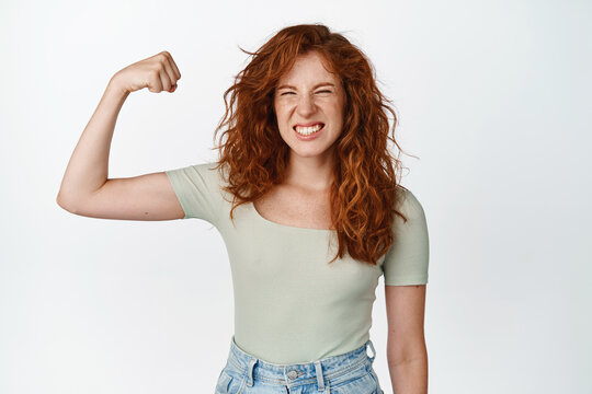 Image Of Sassy Redhead Teenager Flexing Biceps, Showing Muscle On Arm And Looking Happy, Girl Power Gesture, Feeling Strong, Standing Over White Background