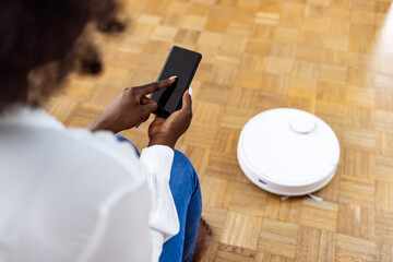 Girl turning on robot vacuum cleaner. Young woman relaxing while robot vacuum cleaning the floor. Woman turns on smart robot vacuum cleaner. Smart technology concept.