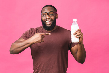 Portrait of young african american black man holding bottle of milk isolated over pink background. Healthy food concept.