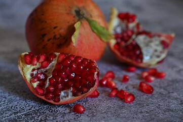 The pomegranate, whole and broken into pieces, lies on a wooden plate