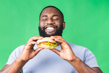 Hungry young african american black man eating hamburger isolated over green background. Diet concept.