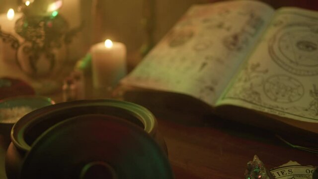 Witch cooking potion elixir close-up. Table with spellbook for making rite. Herbs, burning candles, crystal magic ball for sacrifice. Halloween theme, full moon, witchcraft. 