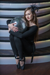 A girl in pointe shoes is sitting on the stairs and holding a mirror ball. A dancer at a musical rehearsal.