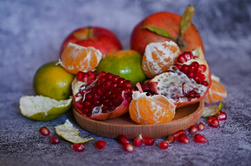 A pomegranate, whole and broken into pieces with other fruits, lies on a marble table