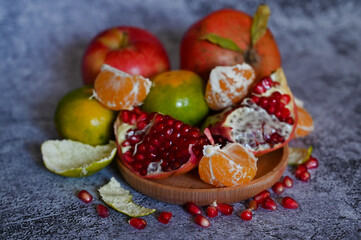 A pomegranate, whole and broken into pieces with other fruits, lies on a marble table