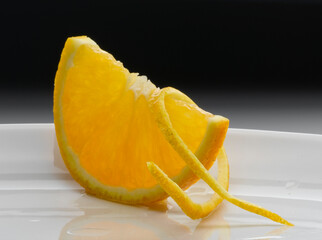 Naranja cortada en gajos con corteza sobre fondo negro. Orange cut into wedges with rind on a black...