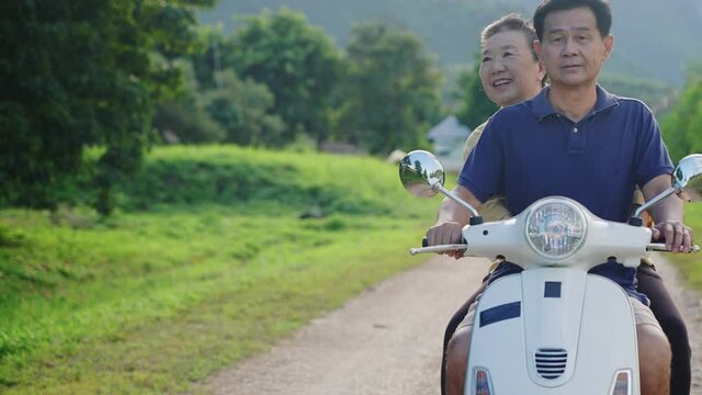 Happy Asian Senior Couple Riding Scooter Around Tropical Island, A Female Elderly Having Fun With Exploring A Beautiful Natural Travel Destination On Motorcycle With Her Husband, Relaxing On Weekend